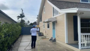 "a man providing house washing via pressure washing the vinyl siding of a house in Naples FL"