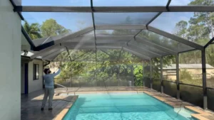 "a man using the soft wash method to provide lanai cleaning service and clean a lanai enclosure with low water pressure and special detergents"
