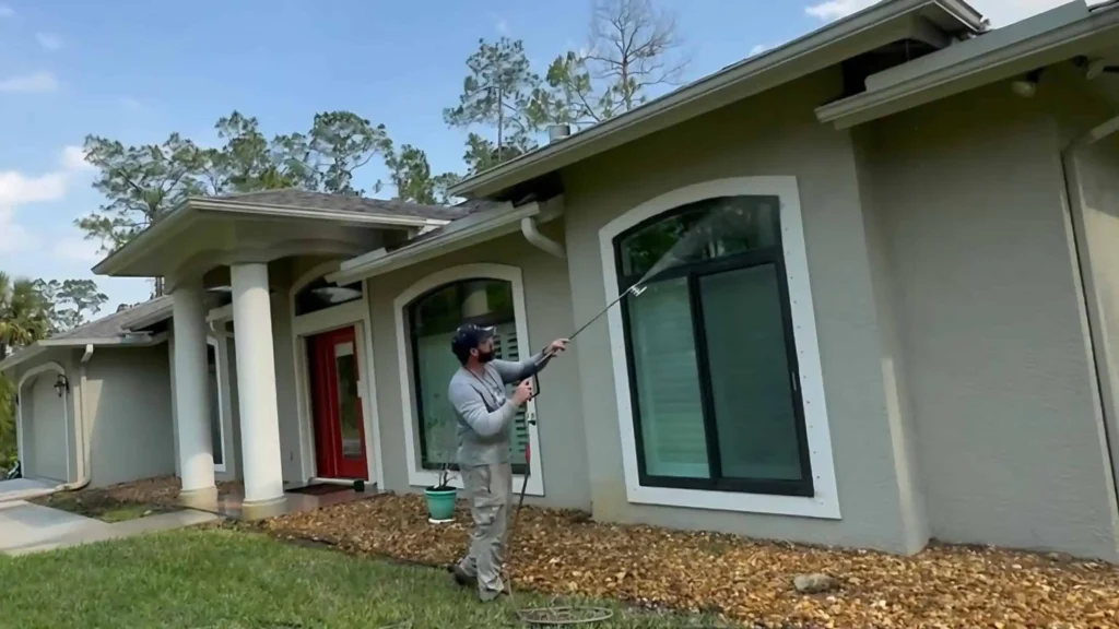 "A professional in beige pants and a gray shirt providing pressure washing services on the exterior wall"