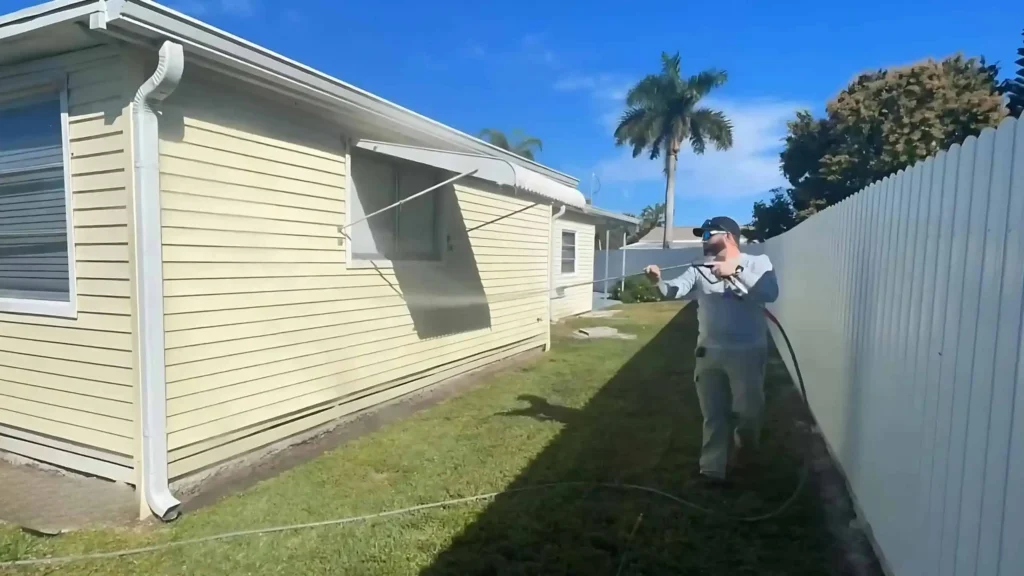 "a man professionally pressure washing the vinyl siding of a house using low pressure to remove grime"